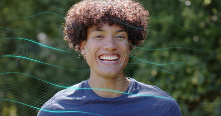 Smiling man wearing navy crew-neck shirt facing camera in park, with stud earrings and teal overlay....