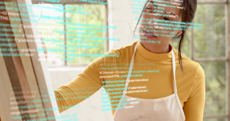 Reaching woman wearing mustard turtleneck and apron tracing code overlay on pane at home studio. Painter, workspace, glass, easel, sunlit, window, digitalの写真素材