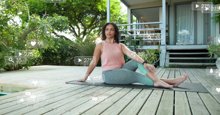 Twisting adult woman in pink top, leggings on dark mat on wooden deck, showing overlays, smartwatch....