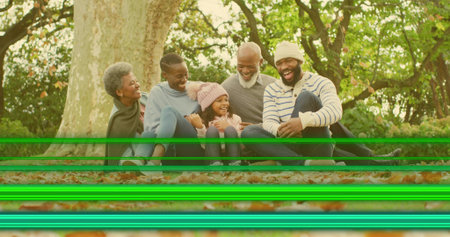 Sitting family wearing sweaters on leafy ground by tree trunk, showing green scan lines. Multigenerational, park, autumn, outdoors, rustic, candid, togetherの写真素材