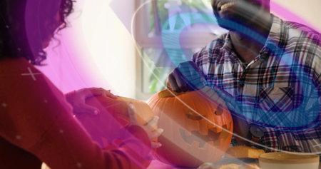 Carving pair wearing plaid shirt and sweater working at home table with carved pumpkin, tools, guts. Jackolantern, duo, daylight, window, cozy, crafting, handmadeの写真素材