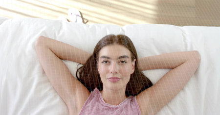 Lying woman wearing sleeveless pink top, resting in bedroom on bed with pillow and blind stripes....