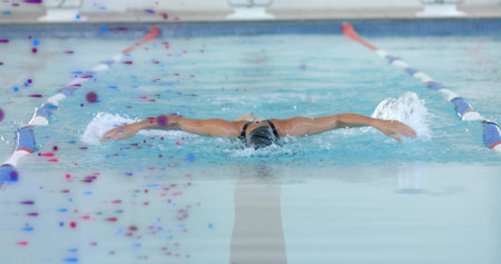 Cutting female swimmer in dark one-piece, swim cap and goggles in pool between dividers, splashing. Athlete, competition, training, lap, water, lane, splashの写真素材