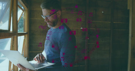 Typing man using laptop by window in wood studio in blue sweater, glasses, magenta overlay, cords. Remote, workstation, focus, bearded, spectacles, computer, daylightの写真素材