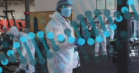 Spraying female worker wearing full PPE disinfecting fitness center with fogger, DNA helix overlay. Sanitation, gym, cleaning, sprayer, disinfection, biohazard, safetyの写真素材