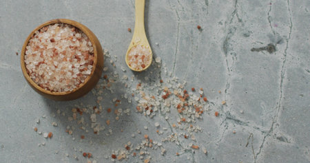 Displaying round wooden bowl holding coarse pink salt on cracked gray slab, small spoon, copy space. Flatlay, stone, crystals, rustic, minimalist, texture, seasoningの写真素材