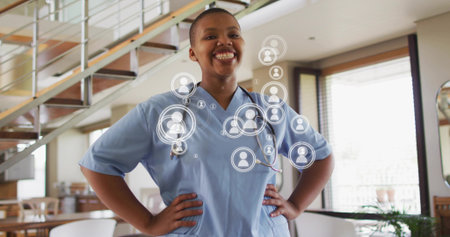 Standing nurse wearing light blue scrubs and stethoscope in modern home, with digital overlays. Healthcare, clinician, professional, female, connectivity, networking, telehealthの写真素材