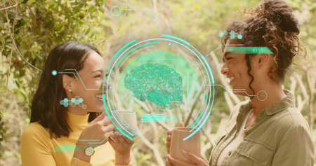 Holding ceramic mugs, two women wearing mustard top olive shirt discussing in garden. Pair, casual, outdoors, patio, greeneryの写真素材