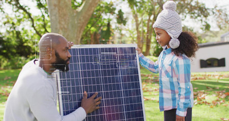 Holding large solar panel, mid adult man and girl steadying in backyard, with beanie and sweater. Photovoltaic, energy, family, parent, child, outdoors, yardの写真素材