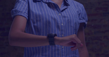Pointing, woman adjusting smartwatch on left wrist at brick wall in blue shirt under blue light. Moody, lighting, wearable, device, striped, studio, lifestyleの写真素材
