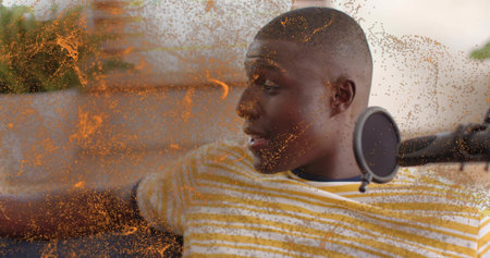 Reclining man in yellow striped tee recording on sofa at home, with mic and pop-filter, orange-dust. Podcast, host, creator, microphone, lounge, broadcast, promoの写真素材