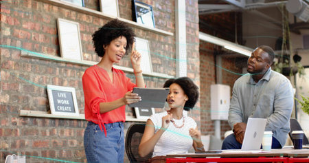 Presenting woman in red blouse holding tablet and pointing to tablet at office, with laptop. Collaboration, brainstorming, coworking, industrial, modern, creative, focusの写真素材