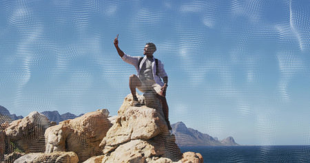 Taking hiker wearing shorts and hiking shoes holding phone high on rocky coast, with backpack. Coastal, rugged, outcrop, ocean, horizon, sunny, solitudeの写真素材