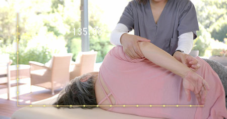 Helping therapist in gray scrubs guiding patient in pink top on padded table near windows, overlay. Physiotherapist, elderly, rehabilitation, mobility, manual, therapy, glassの写真素材
