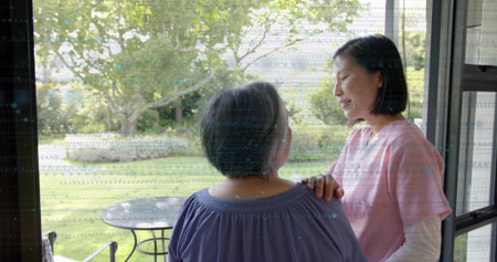 Standing mother and daughter touching shoulder at sliding glass door to garden, pink scrub top....