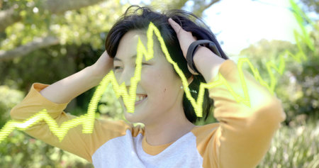 Adjusting woman in raglan tee touching headset in sunny park with fitness tracker and neon waveform....