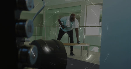 Performing one-arm dumbbell row man wearing light T-shirt, dark pants on bench in gym with towel. Fitness, strength, weights, athletic, focus, lighting, glassの写真素材