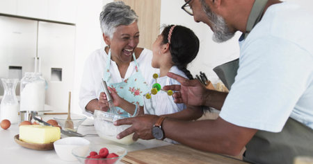 Mixing seniors and child in aprons preparing cookies at kitchen island with bowl and cutters....
