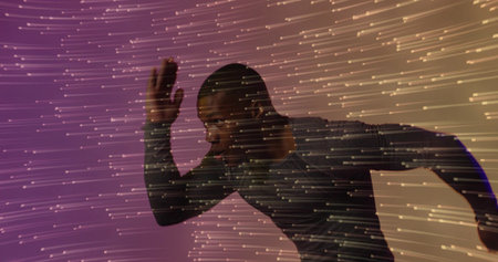Sprinting adult male leaning forward in studio, wearing fitted athletic top with projected streaks....