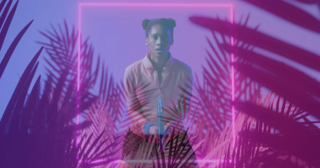 Posing model in zipper jacket, holding cylinder in neon frame studio with magenta purple palms. Moody, gradient, silhouette, tropical, foliage, glow, fashionの写真素材