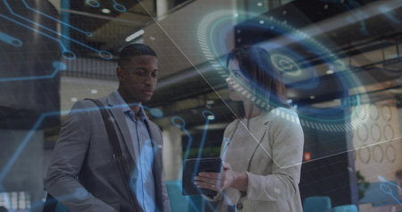 Presenting woman in blazer and man with shoulder strap viewing tablet in office atrium, with HUD....