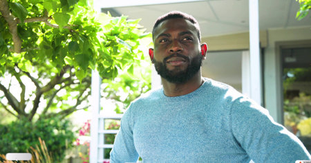 Standing man with trimmed beard gazing upward on front porch, wearing light blue knit sweater....