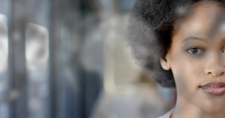 Showing woman through glass in lobby, blurred vertical frames, stud earring, light top, copy space. Closeup, portrait, natural, curly, hair, window, reflectionsの写真素材
