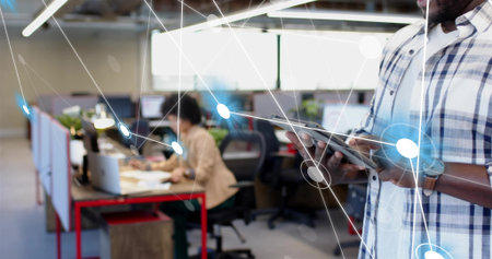 Holding tablet, man in plaid shirt checking network overlay in open-plan office, copy space. Workspace, collaboration, technology, networking, overlay, monitors, plantsの写真素材