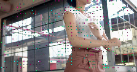 Standing woman adjusting chain necklace in studio by windows, white ribbed top, pink pants, dots. Industrial, warehouse, loft, daylight, sunlit, scaffolding, beamsの写真素材