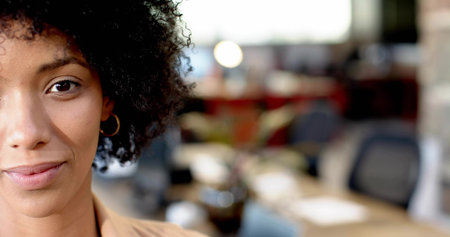 Posing office woman wearing beige blazer, hoop earring, with desks and monitors, copy space. Headshot, professional, workspace, modern, minimalist, warm, bokehの写真素材