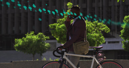 Talking on phone, commuter standing at plaza, wearing blazer, holding white bike with coiled lock. Bicycle, smartphone, urban, professional, outdoor, cityscape, sunlightの写真素材
