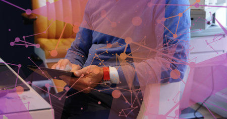 Holding tablet, mature adult man wearing blue sweater tapping screen in office with network overlay. Professional, workspace, modern, digital, focus, productivity, businessの写真素材