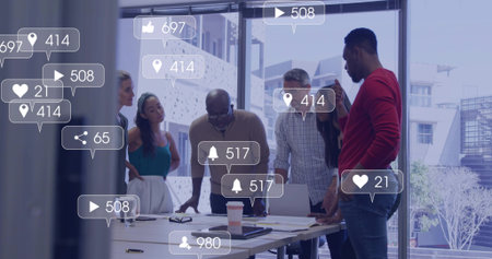 Leaning team of six staff reviewing layouts at office table, in business attire with social icons. Collaboration, colleagues, conference, boardroom, urban, daylight, devicesの写真素材