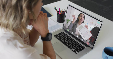 Watching woman wearing blouse and watch leaning on desk, viewing laptop with documents, copy space....