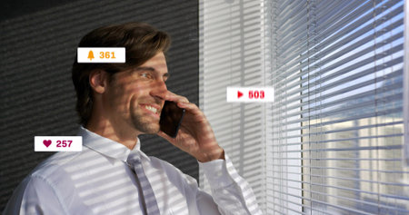 Holding smartphone, man smiling and listening by window blinds, white shirt and tie, notifications....