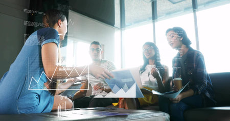 Presenting woman in blue dress leaning and showing tablet with data overlays in office lounge. Collaboration, teamwork, meeting, conference, insights, metrics, visualsの写真素材