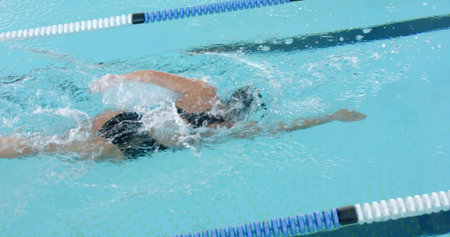 Swimming mature woman pulling through pool lane with dividers, wearing dark swimsuit, cap, goggles. Freestyle, athlete, water, splash, turquoise, training, dynamicの写真素材