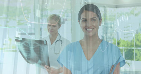 Smiling nurse in blue scrubs standing in clinic, physician in white coat reading chest xray, charts. Dataviz, collaboration, healthcare, sunlit, facility, nature, analyticsの写真素材