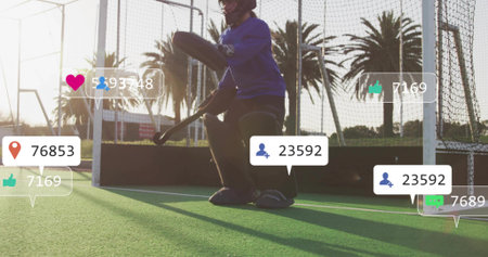 Crouching goalkeeper wearing full pads preparing to save at goal on fenced turf, social overlays....