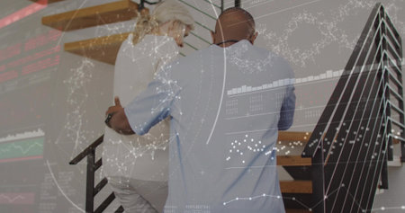 Adult man blue shirt supporting senior woman white blouse climbing wooden stairs at home with HUD. Caregiver, elder, mobility, staircase, residential, overlay, augmentedの写真素材