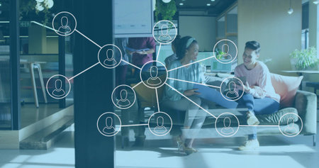 Discussing team wearing casual workwear, sharing laptop and tablet in modern office, network icons. Collaboration, teamwork, coworking, workspace, lounge, glass, plantsの写真素材