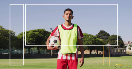 Standing player wearing striped jersey neon bib on field, holding blackwhite soccer ball near poles....