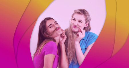 Posing two women in pink-blue tops making hair mustaches in studio white-backdrop magenta-to-yellow. Friends, duo, gradient, abstract, vibrant, campaign, brandingの写真素材