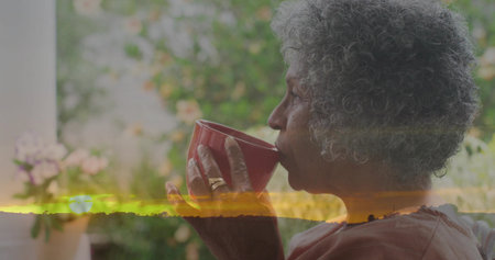 Sipping senior African-American woman in rose-top on porch, holding mug, sunset overlay, copy space. Elderly, outdoor, garden, veranda, greenery, calm, softの写真素材