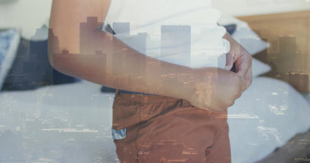 Standing boy wearing white top and rust shorts, clasping abdomen on bed, city skyline overlay. Child, portrait, urban, doubleexposure, bedroom, headboard, advertisingの写真素材