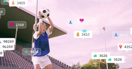 Preparing female soccer player holding soccer ball overhead at sideline, in blue bib. Athlete, stadium, outdoor, throwin, training, floodlights, pastelの写真素材