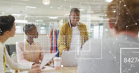 Presenting man in mustard jacket leaning on laptop in office with clothing rack and measuring tape. Collaboration, presentation, design, garments, samples, hud, overlayの写真素材