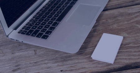 Showing silver laptop with keyboard, trackpad on left side of worn tabletop, with white cards. Workspace, desk, wood, grain, texture, minimalist, flatlayの写真素材