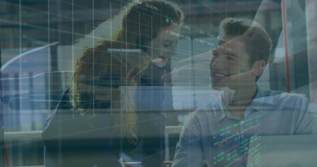 Leaning woman in blazer guiding seated man in shirt over laptop at office, displaying stock charts....