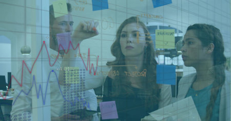 Writing woman in dark top drawing graphs on glass whiteboard at open office with sticky notes....